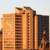 Pixelated image of a tall orange-brown building with vertical lines and windows, set against a light sky background.