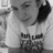 A grayscale image of a person wearing a light-colored shirt with dark text, holding a phone to their ear, with pixelated text at the bottom right.