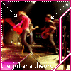 A band performs on stage with a guitarist in pink shirt and red guitar, bassist in dark clothing, and drummer in background; stage lights and pink border frame the scene.