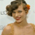 Pixelated image of a person with short dark hair, wearing a light brown sleeveless top, smiling with red lips against a light background.