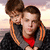 Two people embrace against a sunset sky; one wears a red shirt and dark jacket with orange stripes, the other has brown hair.