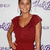 A static image of a person wearing a sleeveless red dress with a V-neckline, standing against a light background with purple cloud-like shapes.