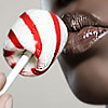 A close-up of a person's mouth holding a red and white striped lollipop with a white stick, against a light gray background.