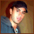 Pixelated portrait of a person with dark hair wearing a blue shirt against a brown background.