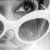 Pixelated grayscale image of a stylized face with large eyes and rounded features, appearing as a low-resolution digital icon.