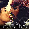 Two people in close proximity with one person wearing a red patterned head covering and the other with dark hair, both facing each other in a dimly lit scene with visible text at the bottom.