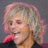 Static pixelated image of a person with light brown hair and pink highlights, wearing dark clothing against a gray background.