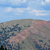 Pixelated landscape with blue sky, white clouds, and a hilly terrain in muted brown and green tones.