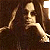 Pixelated figure with long hair reclines against dark background, one arm raised near head.
