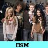 Group of six people standing closely together in a casual pose with a light blue banner displaying 'HSM' at the bottom.