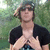 A person in a black shirt and cap stands outdoors with hands clasped, transitioning from crossed arms to a single hand gesture.