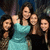 Five people pose together in a group photo; the central figure wears a light blue dress while others wear dark clothing against a dark background.