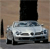 Static image of a silver sedan with dark windows parked in front of a building with a large black rectangular feature on its facade.