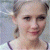 A static image shows a person with light hair tied back, wearing a white top with dark straps against a blurred background.