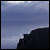 Pixelated static image showing a dark silhouette of a rocky cliff against a gradient sky transitioning from light blue to gray.