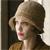 Pixelated profile view of a person with light brown hair, red lips, and a brown garment against a dark and light background.