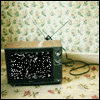 A vintage television set with static on the screen sits on a floral-patterned surface against a matching wallpaper background.