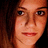 Pixelated close-up of a person's face with light skin tone, dark eyes, and reddish-brown hair against a dark background.
