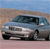 A light blue sedan with dark tinted windows is positioned on a sandy terrain under a clear blue sky.