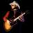 Pixelated image of a person with light hair holding an electric guitar against dark background.