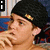 A pixelated image of a person wearing a black beanie with yellow accents, resting their chin on one hand against a blue and red patterned background.
