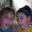 Two people with brown hair pose closely together; one wears a blue headband and yellow top, the other a teal top.