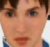Pixelated close-up of a person's face with light skin tone, brown hair visible at top edges, green and blue eyes, and mouth slightly open.