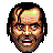 Pixelated face with dark hair, brown skin tones, and a greenish-yellow patch on the forehead against gray background.