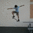 Pixelated image of a person skateboarding with arms outstretched, wearing light blue shirt and dark shorts against textured background.