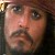 Pixelated close-up of a person's face with light skin tone, dark eyes, and a mustache, set against a dark background with a faint golden element on the left.