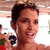 A pixelated close-up of a person with short dark hair, light skin, and a slight smile, wearing a red top against a blurred background with indistinct shapes.