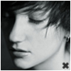 Black-and-white close-up of a person's face in profile, showing closed eyes, dark hair, and a small earring, with a small black X symbol in the bottom-right corner.