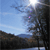 Pixelated landscape with blue sky, scattered clouds, and dark tree silhouettes against a bright sun.