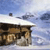 Pixelated static image of a building with a sloped roof under a blue sky with scattered clouds.