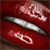 A static image shows a metallic object with a curved shape against a red background, with faint light-colored patterns above and below it.