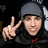 A pixelated image shows a person wearing a dark hooded garment with a red accent, making a peace sign with their right hand against a black background with green text.