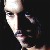 Pixelated close-up of a person's face with light skin tone, dark hair, and dark eyes against a dark background.