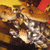 Pixelated static image with warm brown and orange tones, featuring indistinct shapes resembling a figure in motion against a blurred background.