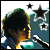 A person with dark hair in profile view, wearing a blue and white striped shirt, singing into a microphone against a teal background with stars.