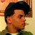 Pixelated close-up of a person with dark hair wearing a dark green beret and green clothing against a light brown background.