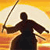 Pixelated silhouette of a martial artist holding a long staff against a gradient sunset background with yellow and orange tones.