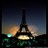 Pixelated static image of a tall dark tower with a glowing base against a gradient sky and blurred lights below.