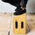 A 4-frame contact sheet animation of a person in black clothing performing actions with a yellow box on a light background.