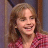 A static pixelated image of a person with light brown hair wearing a red and white checkered shirt, smiling against a blurred background.