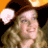 Pixelated image of a person wearing a brown hat with a light-colored brim, holding a white object near their face against a dark background with orange lighting.