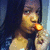 Pixelated image of a person with long dark hair holding a glowing orange object near their mouth against a dark blue background.