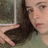 A static image shows a person with dark hair holding an object near their face, set against a blurred background.