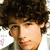 A pixelated portrait of a person with curly dark hair, wearing a dark jacket over a light shirt, with a pink heart symbol appearing on the right side.