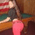 A pixelated figure in a dark top and pink pants sits at a pool table with an American flag backdrop, showing slight motion in the lower right.