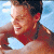A pixelated image of a person with short dark hair, wearing a red shirt, smiling with eyes closed against a light blue background.